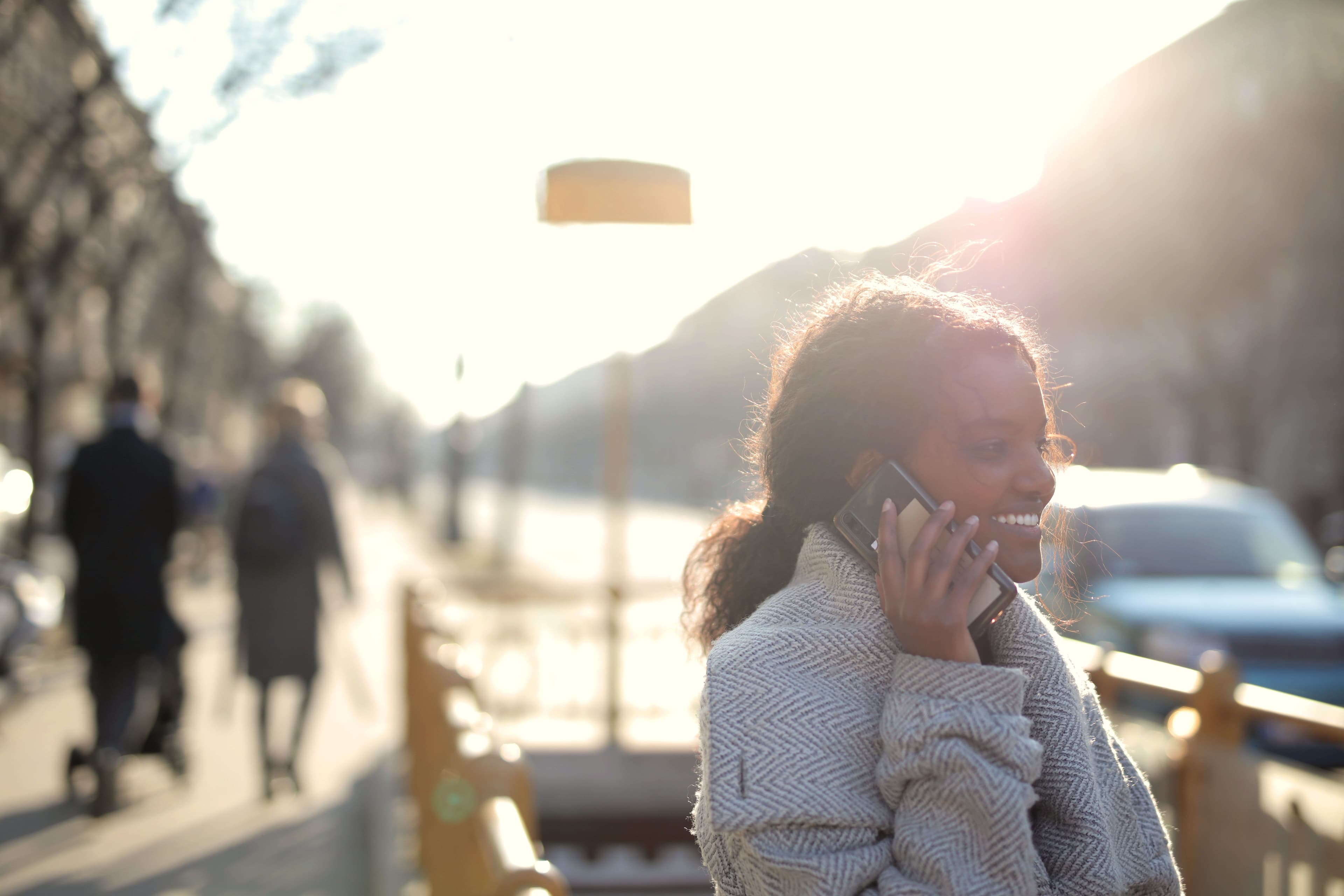 A woman smiling warmly while talking on the phone outdoors at golden hour