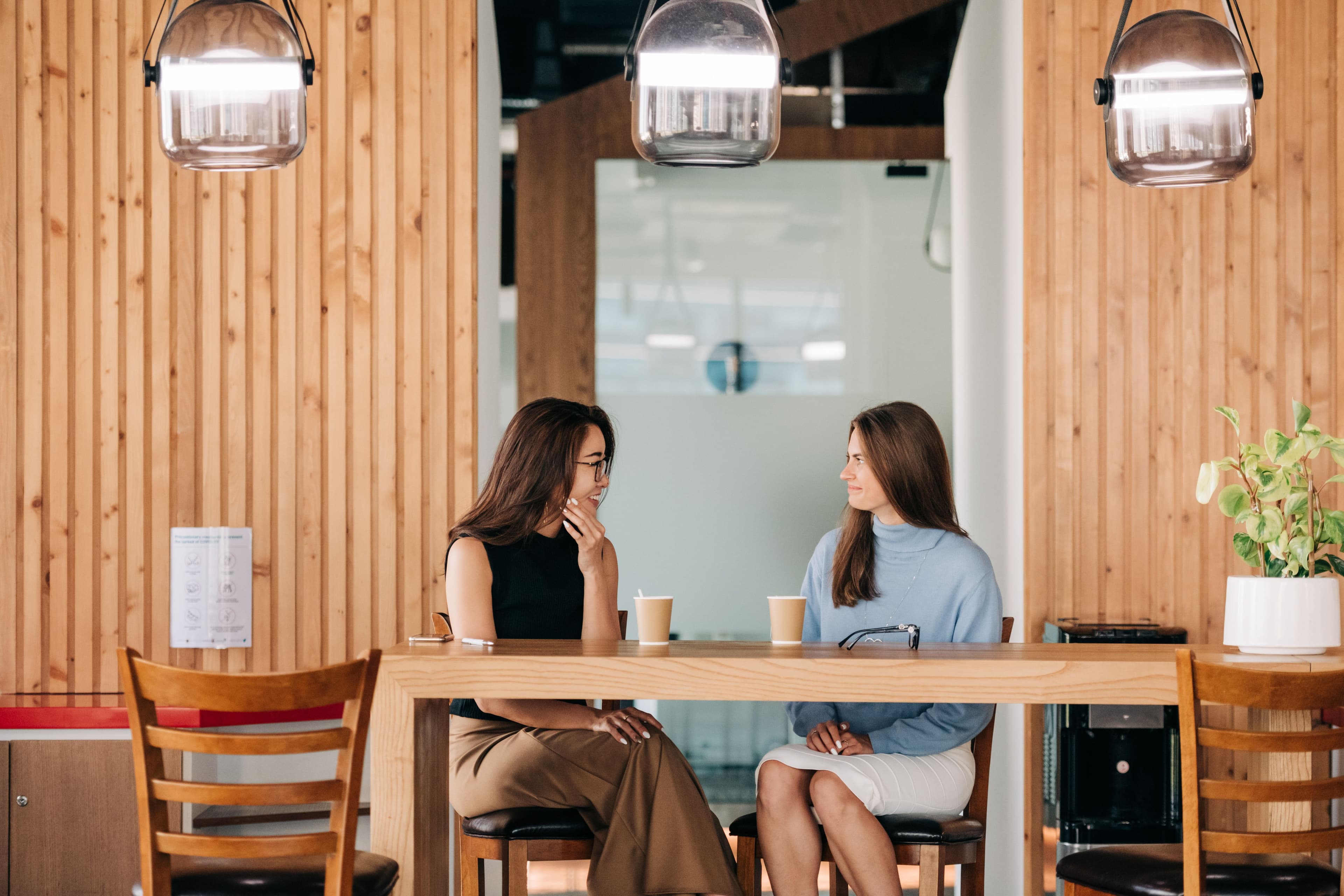 Two women laughing and talking warmly over coffee at a cafe table, representing genuine friendship